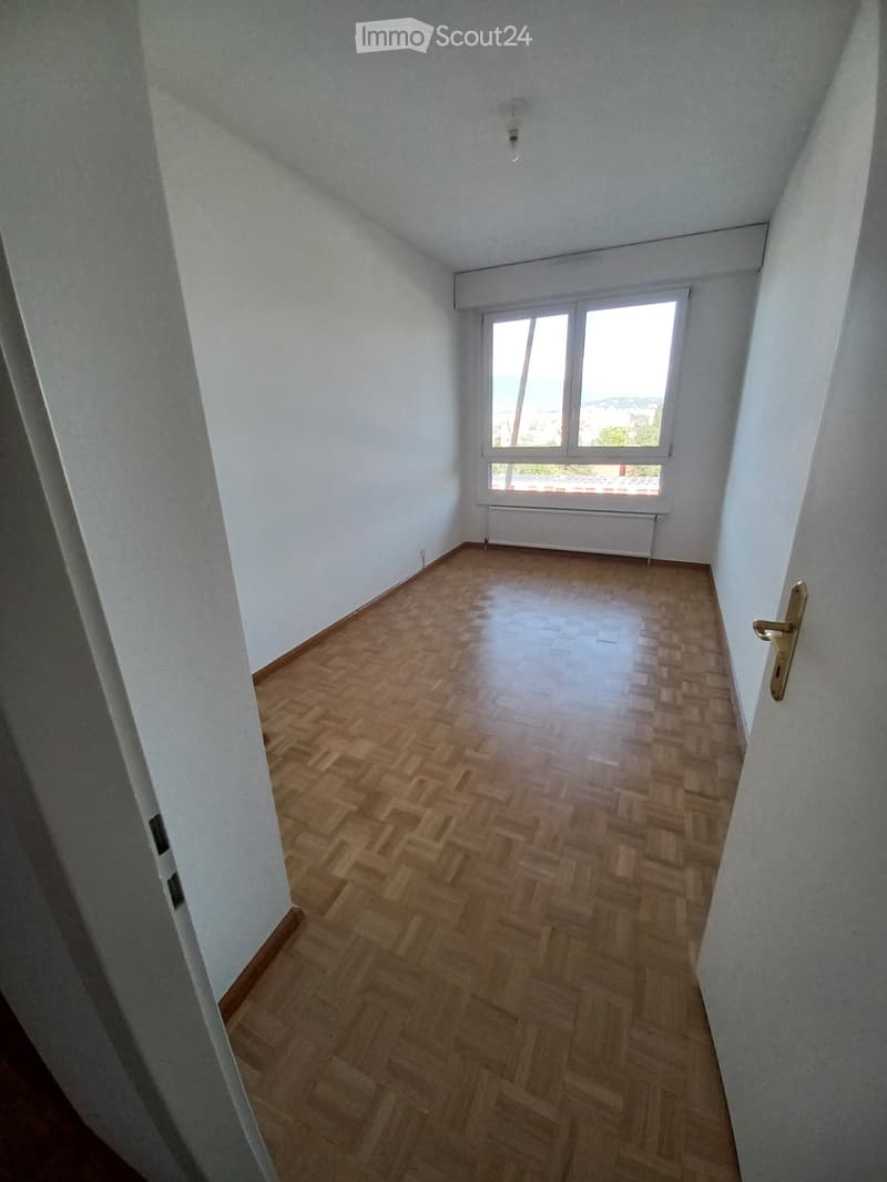Empty room with wooden flooring, white walls, and a large window with a view. No furniture or equipment is present.