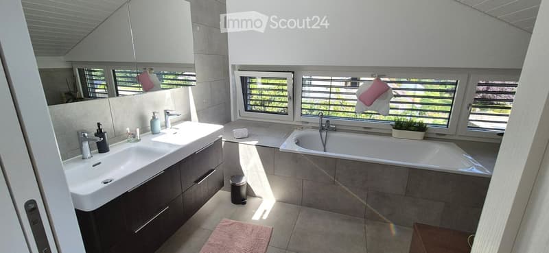 Modern bathroom with double sink, bathtub, large windows, and a small plant on the windowsill.