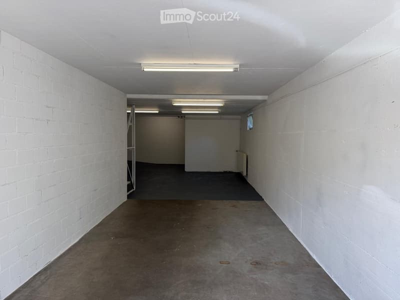 Empty concrete corridor with white brick walls, fluorescent lighting, and a small room at the end.