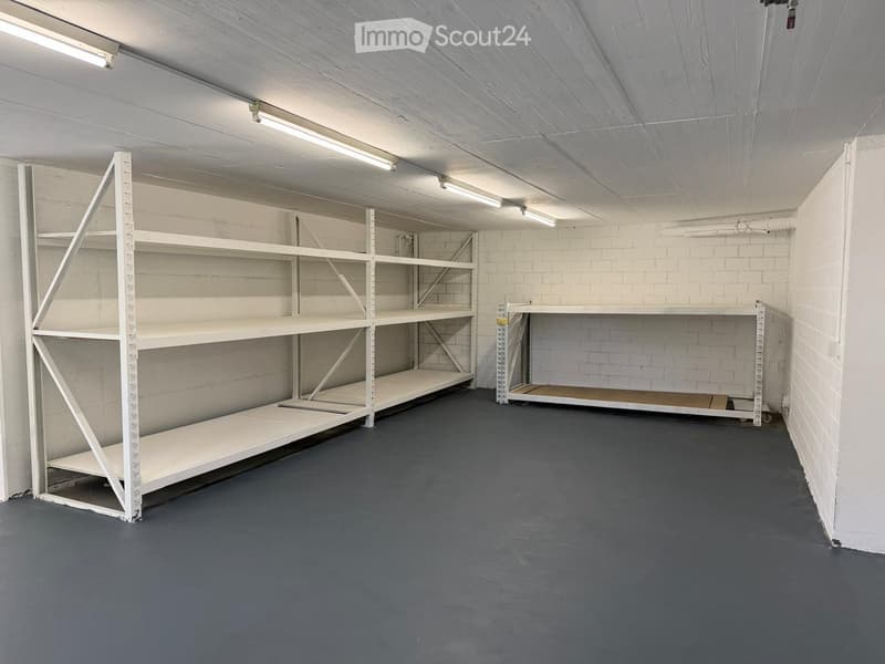 Empty storage room with white metal shelving units and a concrete floor.