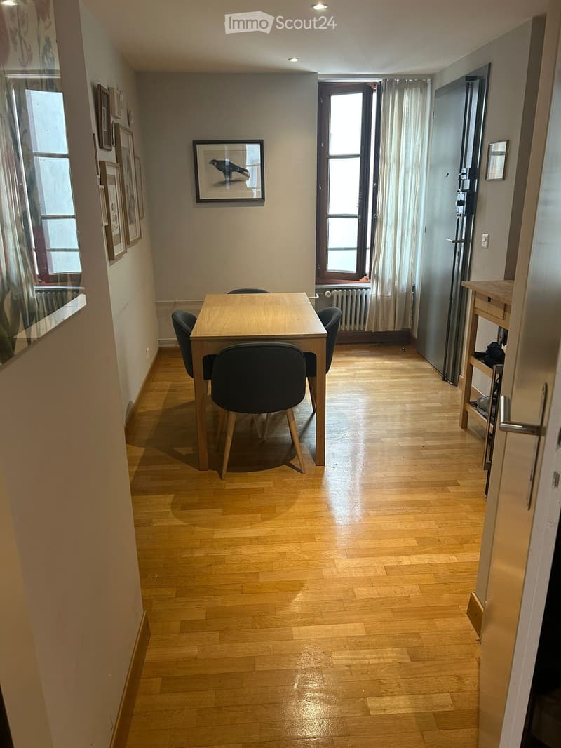 Dining area with wooden floor, table, chairs, and artwork on walls.