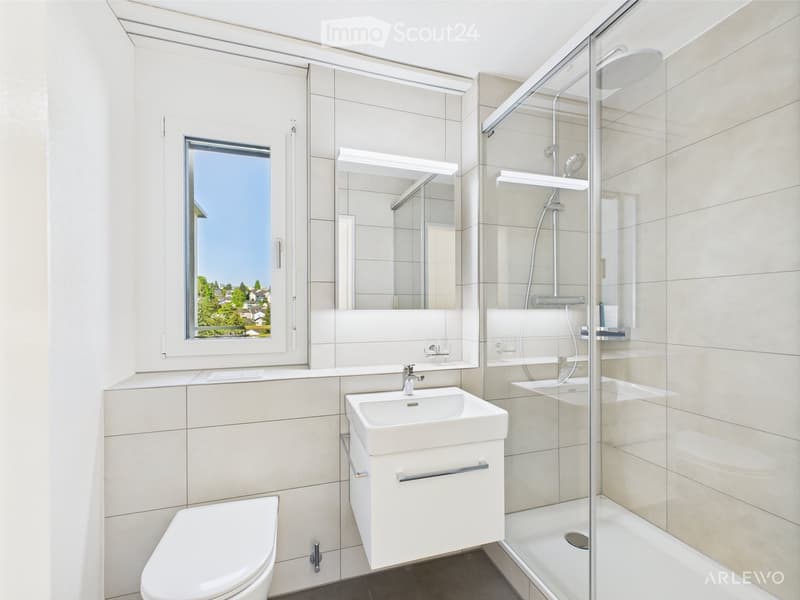Modern bathroom with a toilet, sink, mirror, and walk-in shower with glass enclosure. Features a large window with a scenic view.