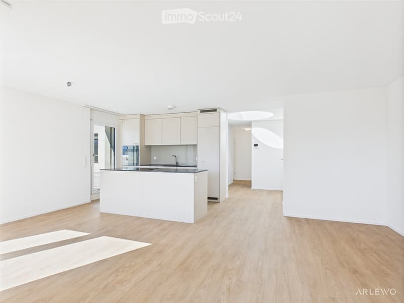 Empty room with white walls, light wooden flooring, and a white kitchen island. No furniture or appliances are present.