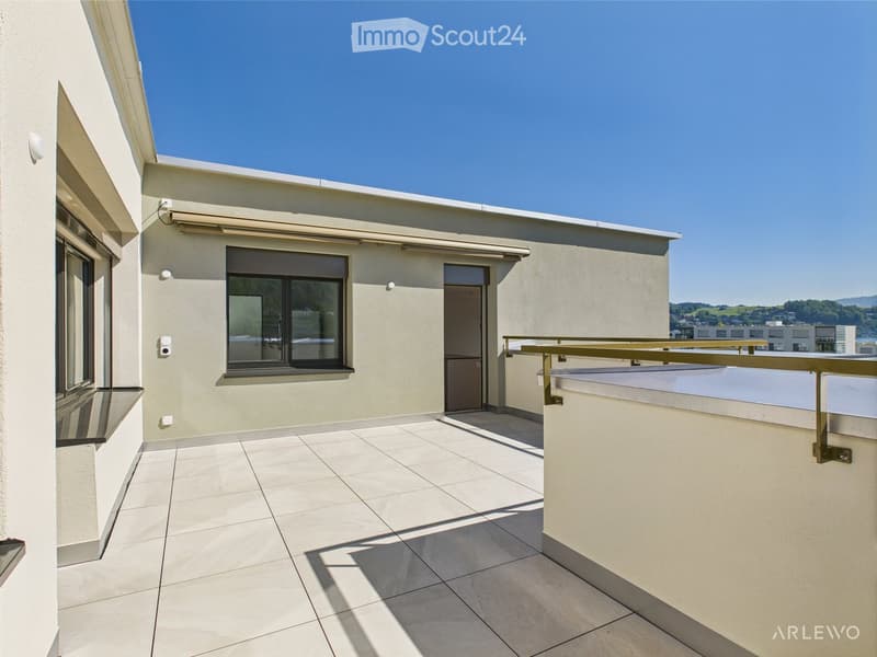 Clean, modern rooftop terrace with tiled flooring, white walls, and a metal railing. Features a large window and a door leading to the interior.
