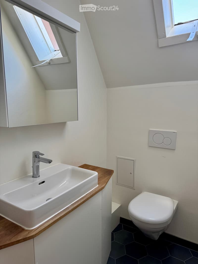 Modern bathroom with a white sink, chrome faucet, and a toilet. Features a wooden countertop and white walls.