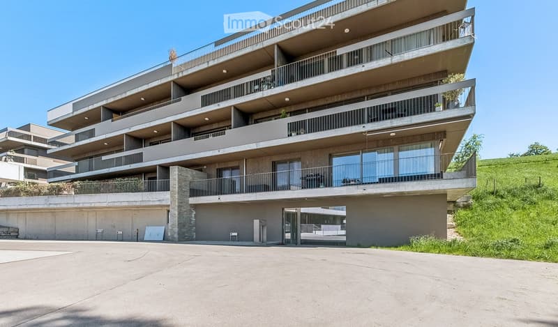 Modern multi-story apartment building with balconies, large windows, and a covered parking area.