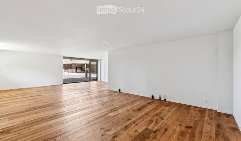 Empty room with light wooden flooring and white walls, featuring a large sliding glass door leading to another space.