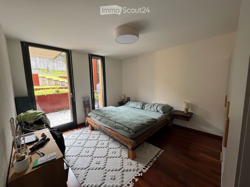 Cozy bedroom with a wooden bed, nightstands, a small table, and a view of a garden through large sliding doors.