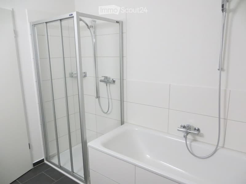Modern bathroom with a white bathtub, glass-enclosed shower stall, and chrome fixtures.