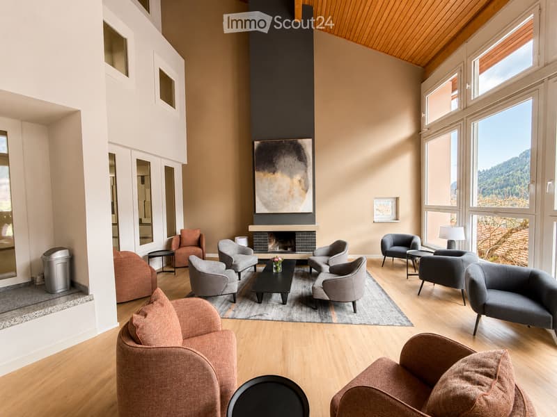 Modern living room with a fireplace, large windows offering a scenic view, multiple seating options including sofas and armchairs, coffee table, side tables, and artwork on the wall.