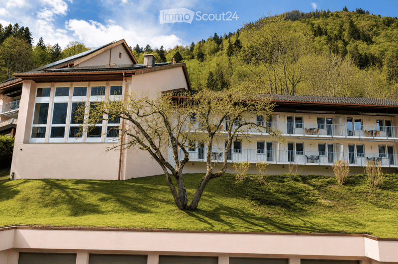 A two-story house with a modern design, featuring large windows, balconies, and a well-maintained lawn in a lush, green setting.