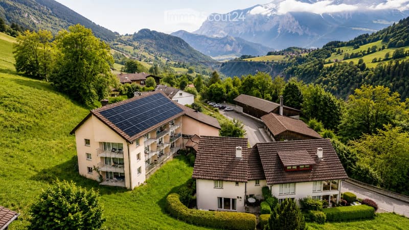 Aerial view of a residential area with multiple houses, surrounded by lush green trees and mountains in the background.