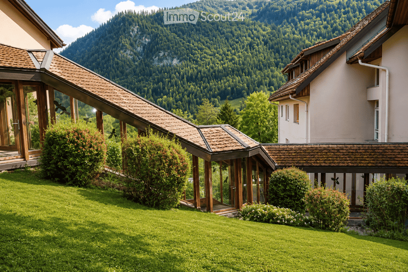 A two-story house with a tiled roof, surrounded by a well-maintained lawn and lush greenery, with a scenic mountain backdrop.