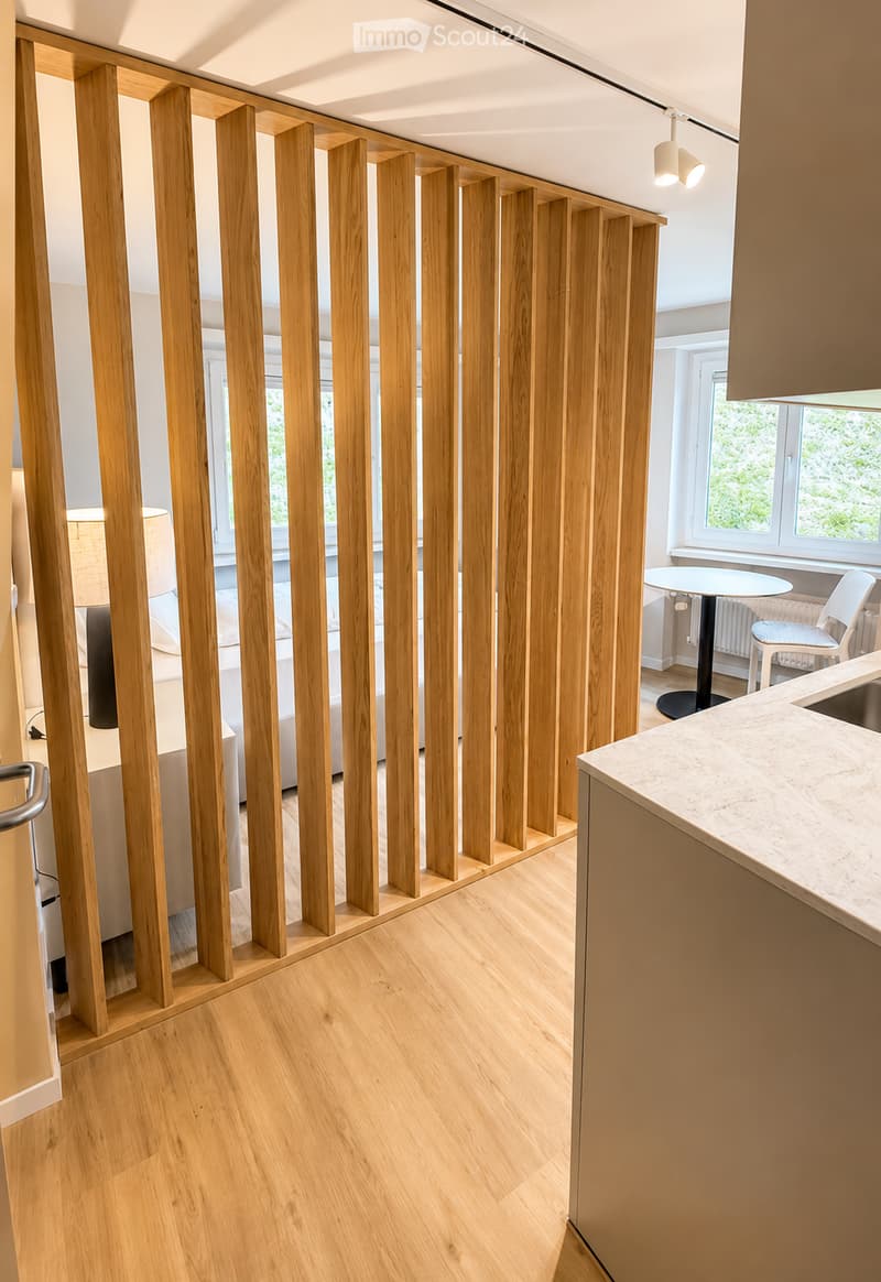 Modern open-plan living and dining area with light wooden flooring, a white sofa, a round dining table with chairs, and a kitchen counter with a sink.