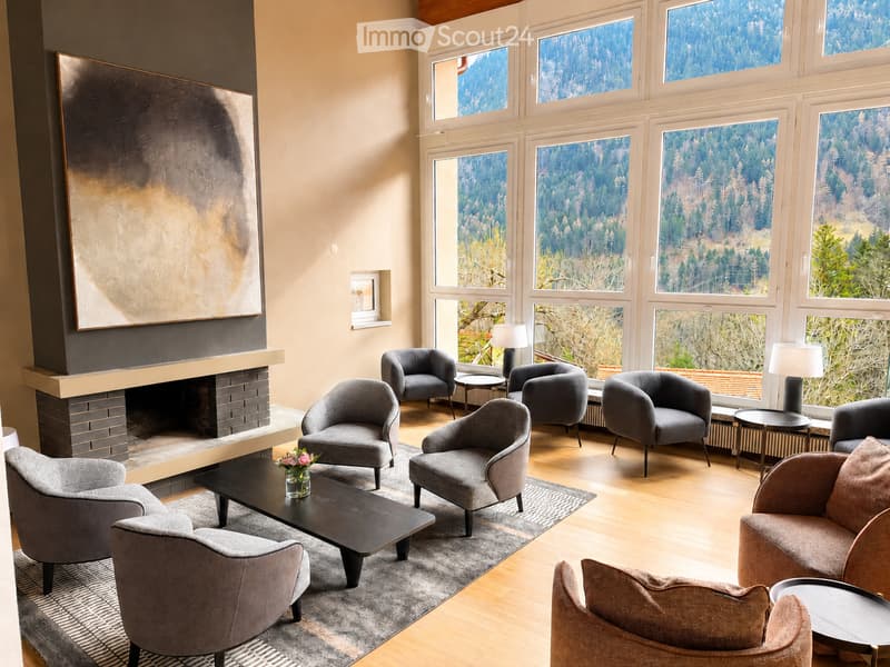 Modern living room with large windows offering a scenic view, a fireplace, several armchairs, a coffee table, and table lamps.