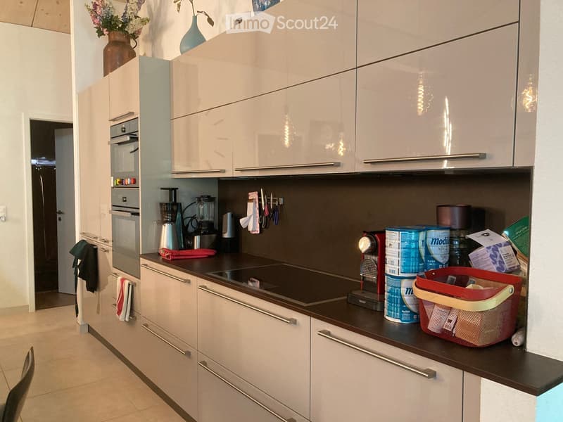 Modern kitchen with white cabinets, stainless steel appliances, and a dark countertop. Visible items include a coffee maker, blender, and various kitchen utensils.