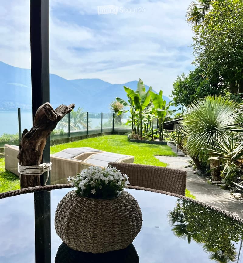 balcony with table and lounge chair, flowers, grassy garden, plants, view of lake and mountains
