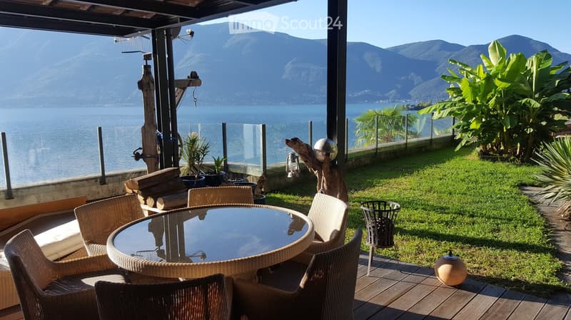 glass railing, wooden deck, round table, chairs, green lawn, ocean view, wooden pillars, fire pit, trees, plants