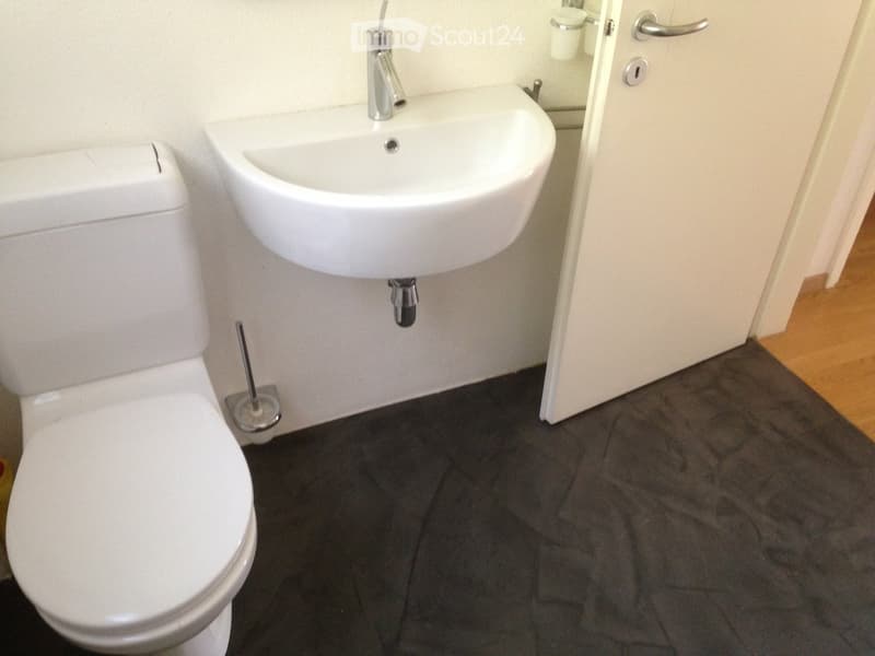 modern bathroom, white toilet, white wall, white countertop, white sink, silver faucet, mirror, toilet brush