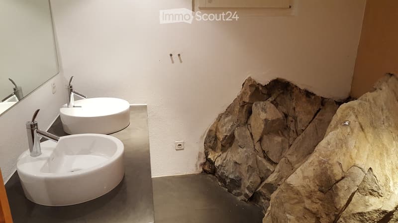 Bathroom with white sink and natural rock wall, double sink, mirror, and faucets, tile flooring