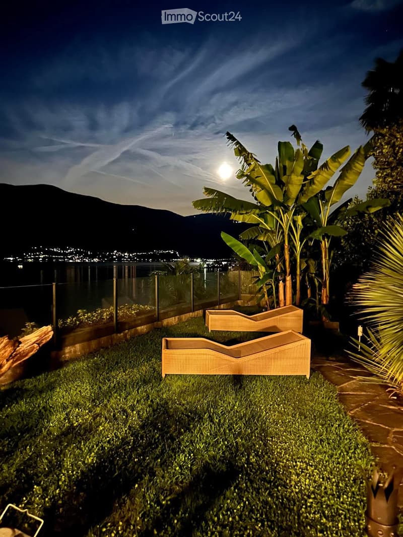 a backyard with two lounge chairs, a full moon, water in the background, mountains in the background, and a clear sky