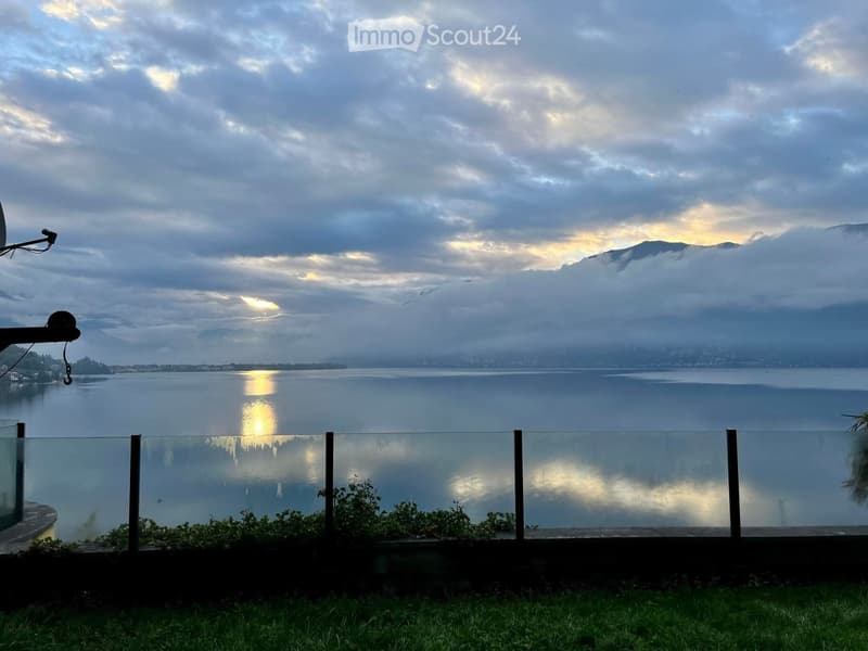 A view of a lake with mountains in the background, a cloudy sky, and a fence.