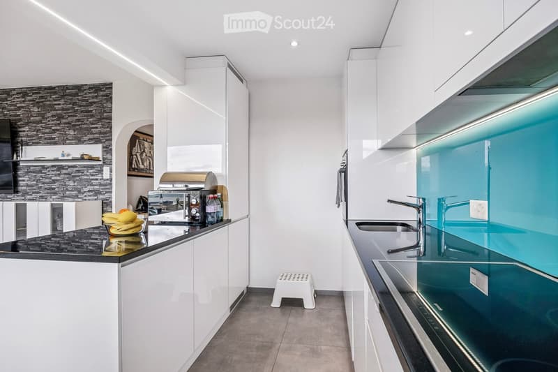 Modern kitchen with white cabinets, black countertops, stainless steel appliances, and a glass backsplash. Features a sink, faucet, and various appliances including a toaster and a fridge.