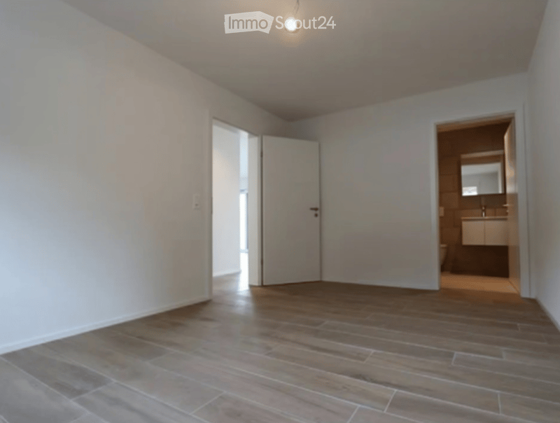 Empty room with wooden flooring and white walls, featuring an open doorway leading to a bathroom.