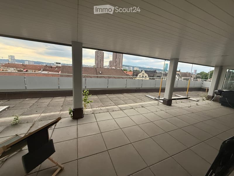 Empty rooftop terrace with tiled floor, metal railing, and a view of the city skyline.