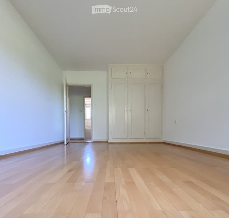 Empty room with light wooden flooring, white walls, and built-in white cabinets. An open doorway leads to another room.
