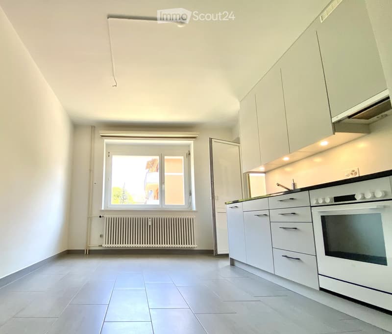 Modern kitchen with white cabinets, a built-in oven, and a window overlooking a view. The space features tiled flooring and a radiator below the window.