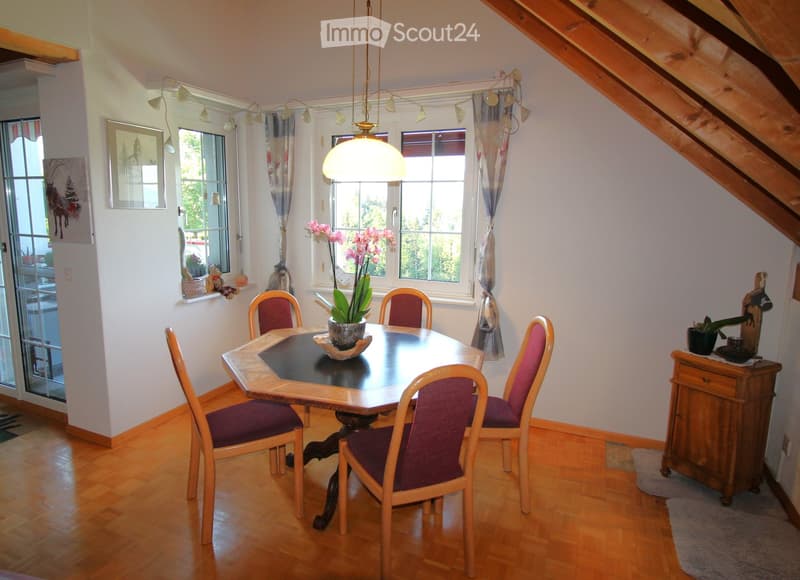 Dining room with wooden floor, round wooden dining table, six chairs, flower pot, cabinet, and picture frame on the wall.