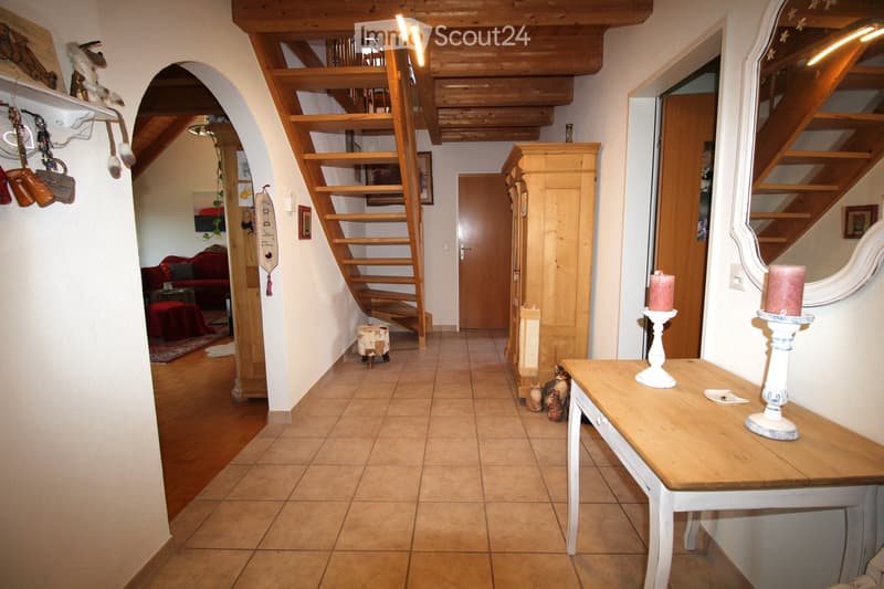 Cozy hallway with wooden staircase, tiled floor, and decorative items including a small table with candles, a cat, and a red sofa visible in the background.