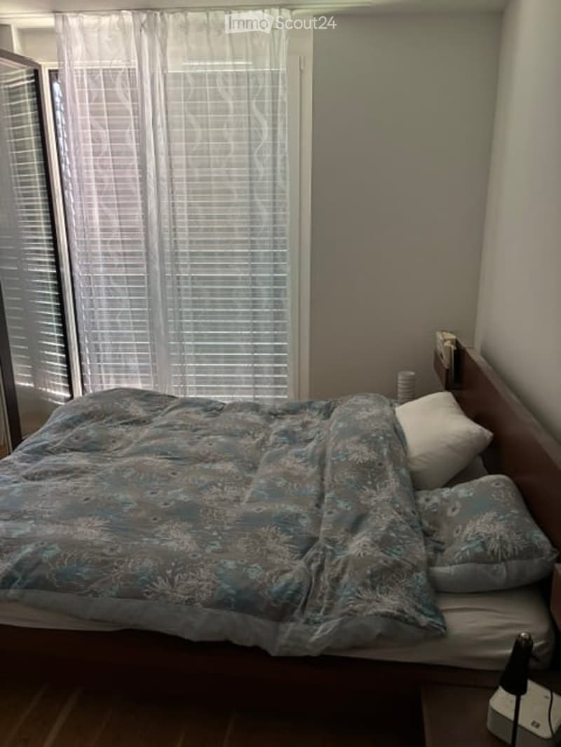 Bedroom with a wooden bed, blue patterned duvet, white pillows, and a nightstand with a lamp.