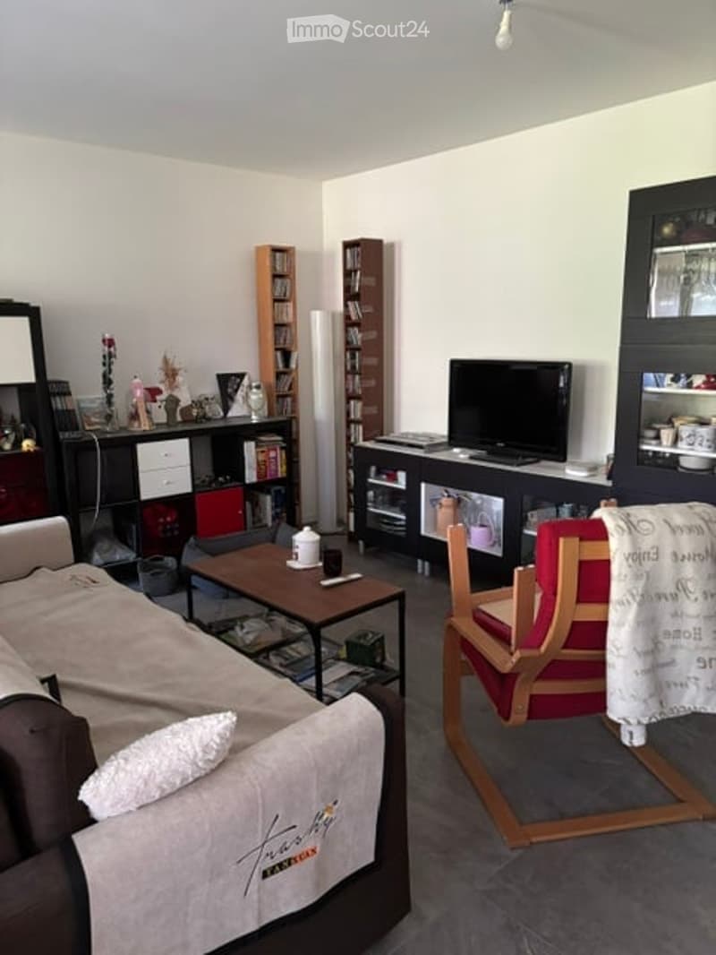 Living room with a beige sofa, coffee table, wooden chair, bookshelf, television, and decorative items on shelves.