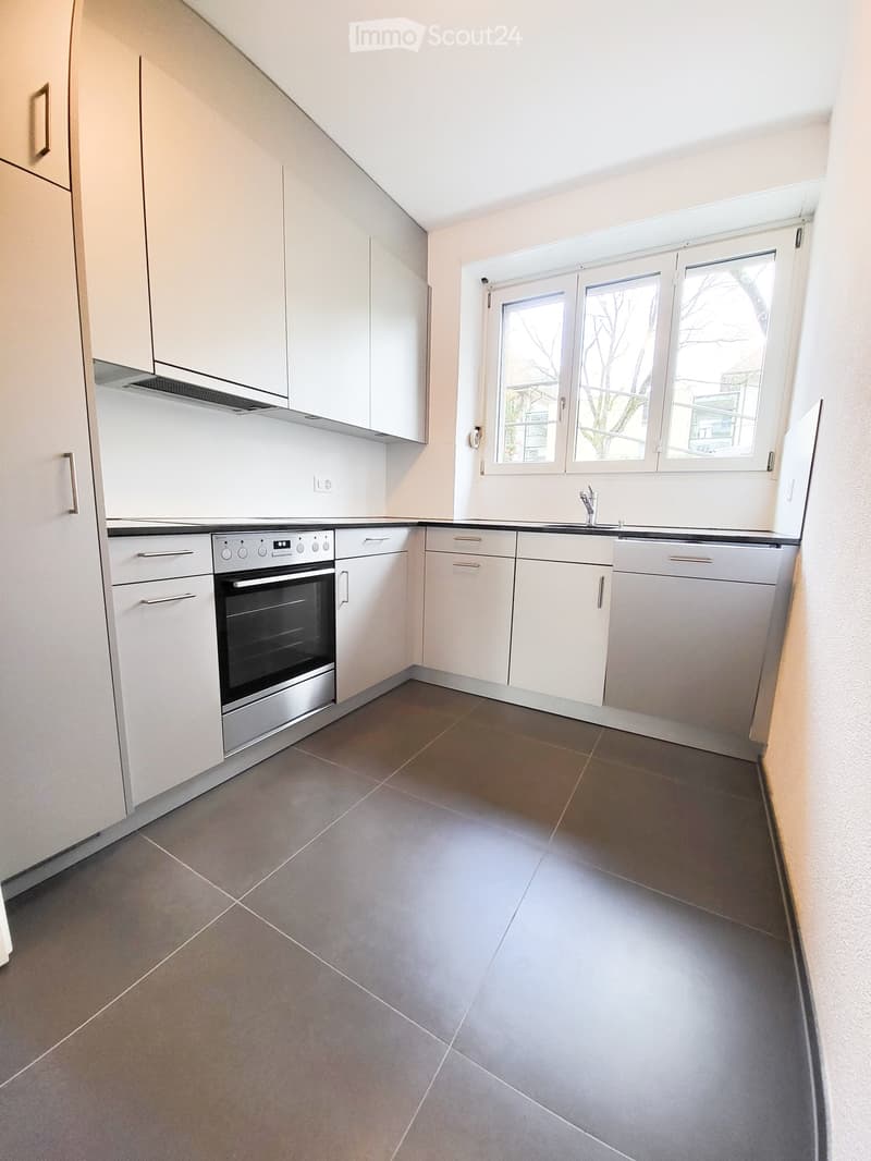 Modern kitchen with white cabinets, stainless steel oven, and grey tiled floor.