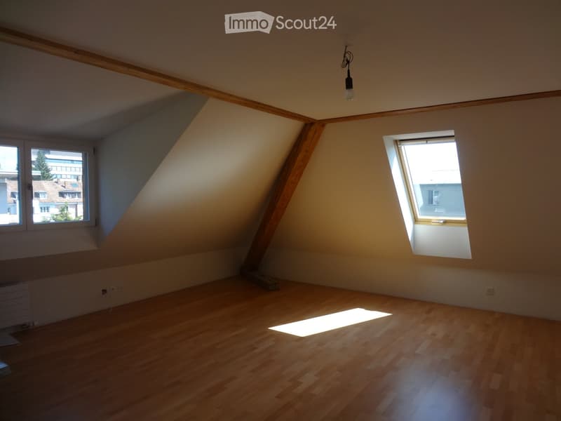 Empty attic room with wooden floors, slanted ceilings, and two windows allowing natural light to enter.
