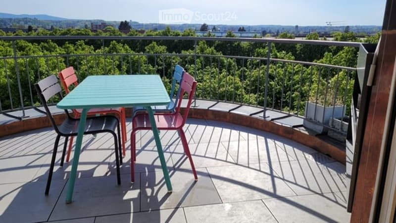 Balcony with a small table and four chairs, overlooking a green landscape with trees and distant cityscape.