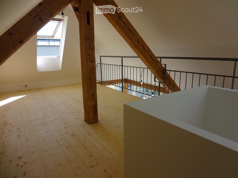 Empty attic space with wooden floors, exposed wooden beams, and a skylight window. A staircase leads to a lower level.