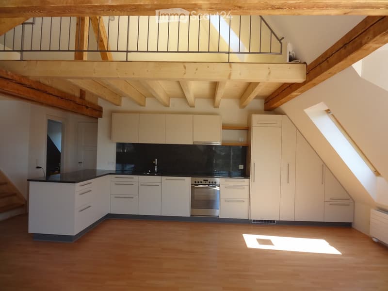 Modern kitchen with white cabinets, black countertop, stainless steel oven, and wooden flooring.