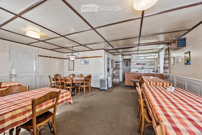 Restaurant or dining area with wooden tables and chairs, checkered tablecloths, a bar area with shelves, and a mirror on the wall.