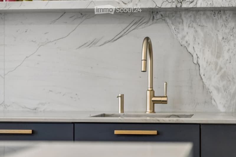 Modern kitchen sink area with a sleek gold faucet, marble countertop, and dark grey cabinets.