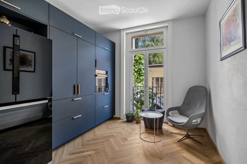 Modern living room with herringbone wooden flooring, grey cabinetry, a sleek grey armchair, a round metal side table, and framed artwork on the wall.