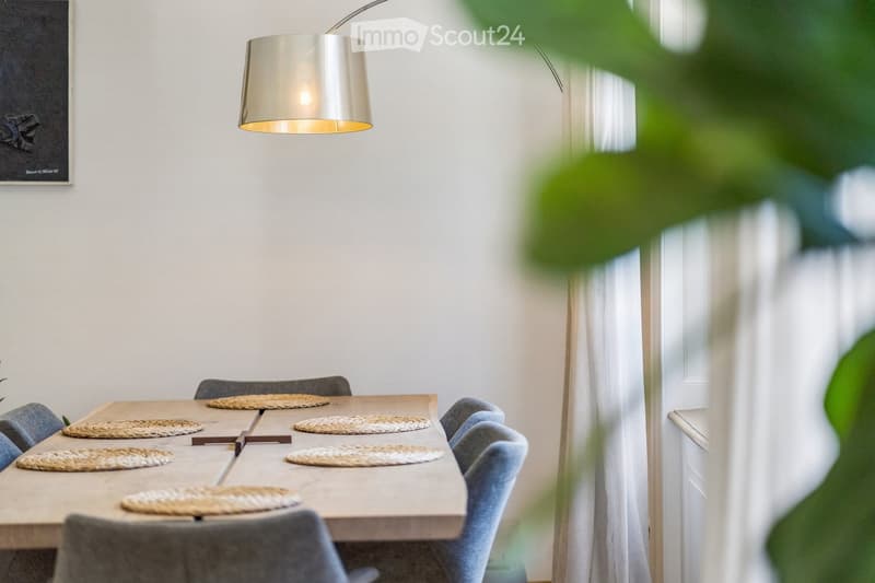 Modern dining area with a wooden table, six chairs, placemats, and a pendant light fixture.