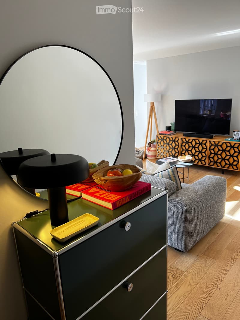 Modern living room with a grey sofa, coffee table, television, side tables, floor lamp, and decorative items including books and a bowl.