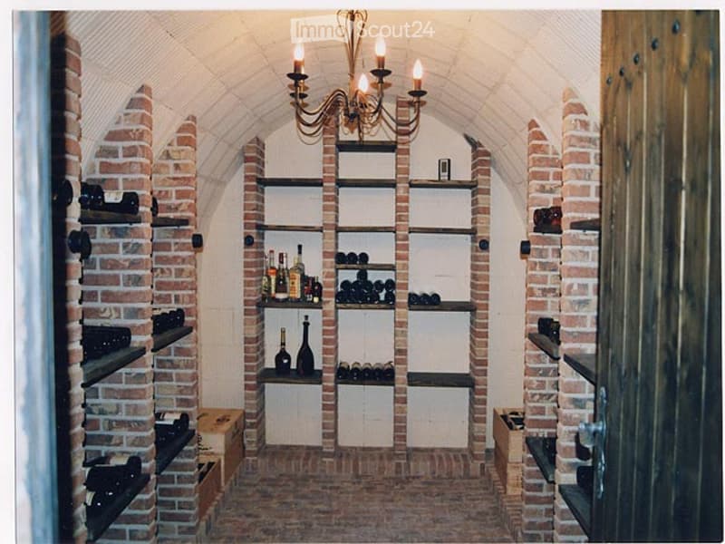 Wine cellar with brick walls, arched ceiling, and shelves filled with bottles and wine racks.