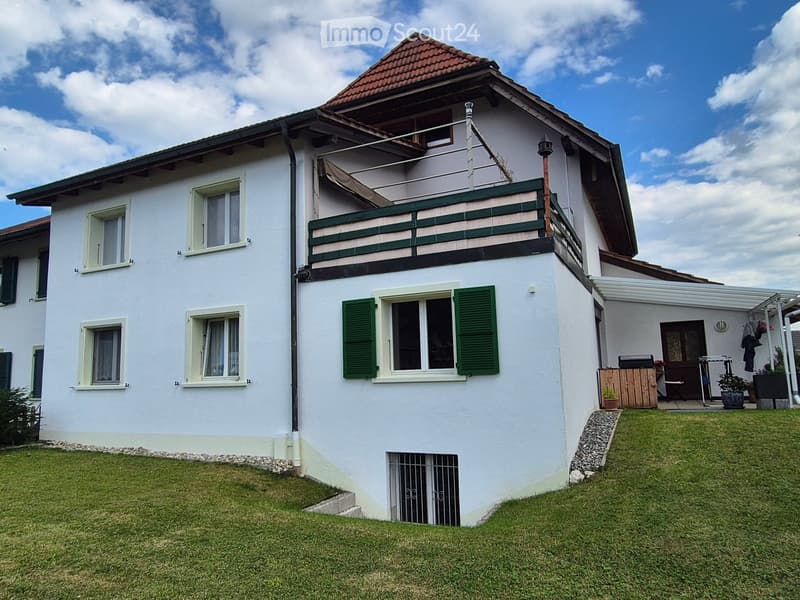 Two-story white house with green shutters, a balcony on the upper floor, and a well-maintained lawn in front.