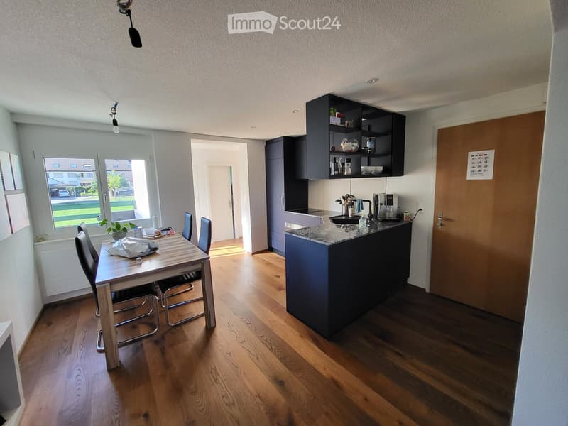 Modern kitchen and dining area with wooden flooring, a dining table with chairs, a kitchen island, and built-in cabinets.