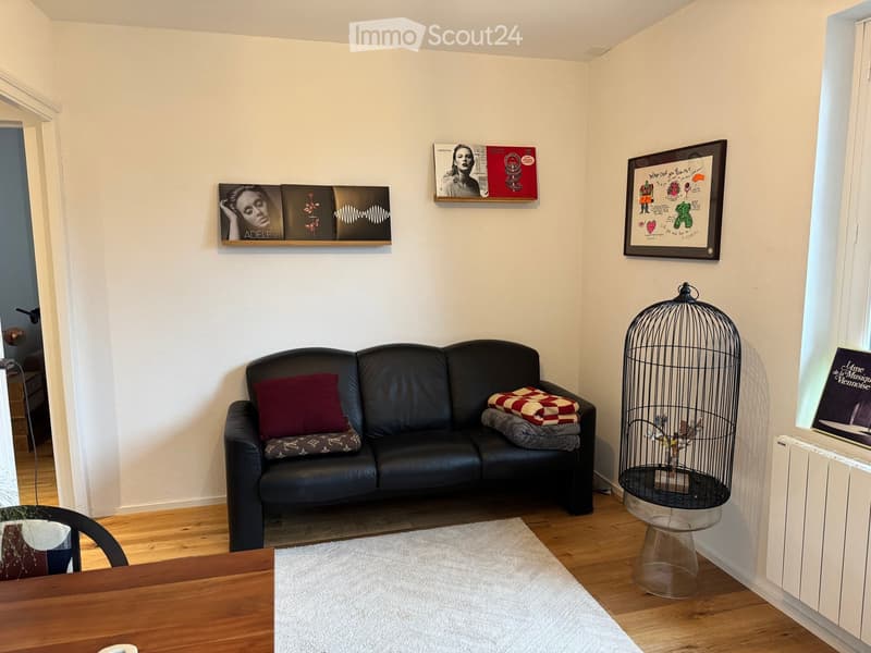 A modern living room with a black leather sofa, a wooden table, a birdcage, and several picture frames on the wall.