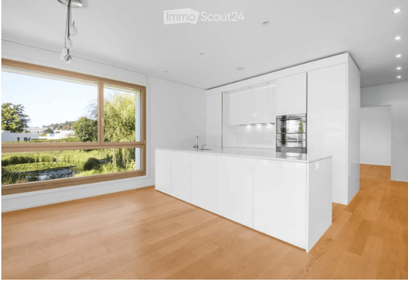Modern kitchen with white cabinets, a central island, and large windows offering a scenic view of greenery outside.